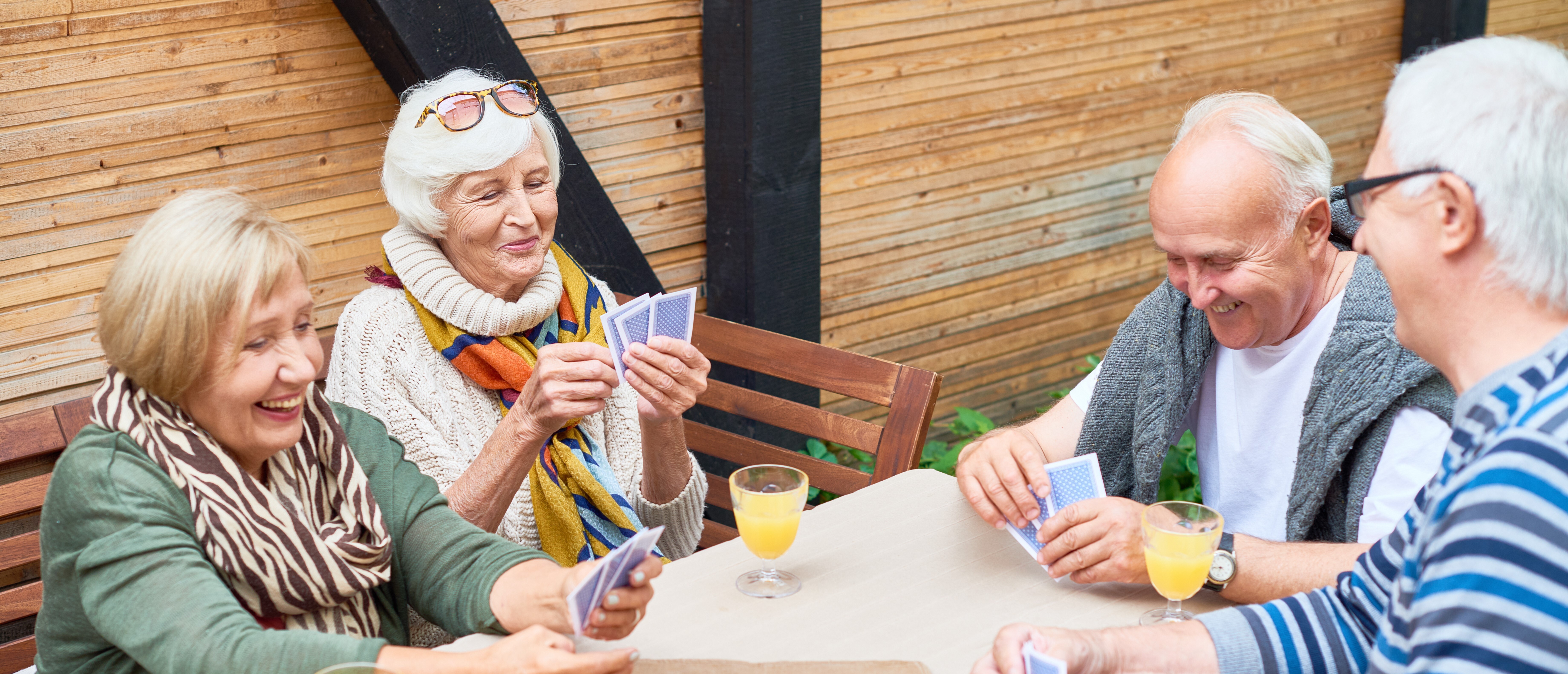 A group of seniors enjoying time outdoors playing a card game around a table.